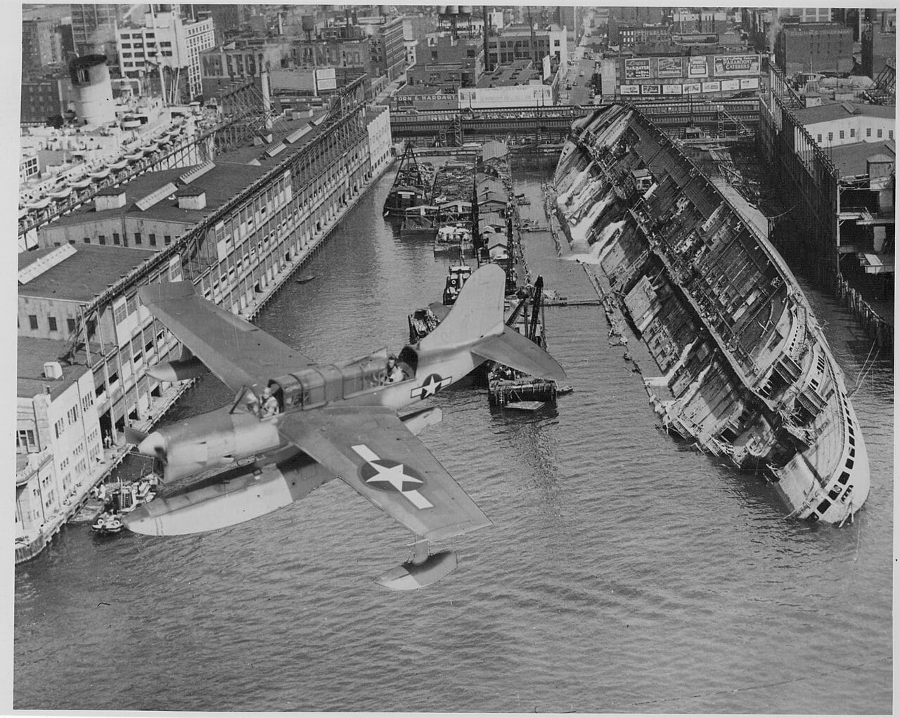 Un Grumman Widgeon de los Guardacostas de EE. UU. sobrevuela los restos del casco del USS Lafayette/Normandie tras el sabotaje en Nueva York 